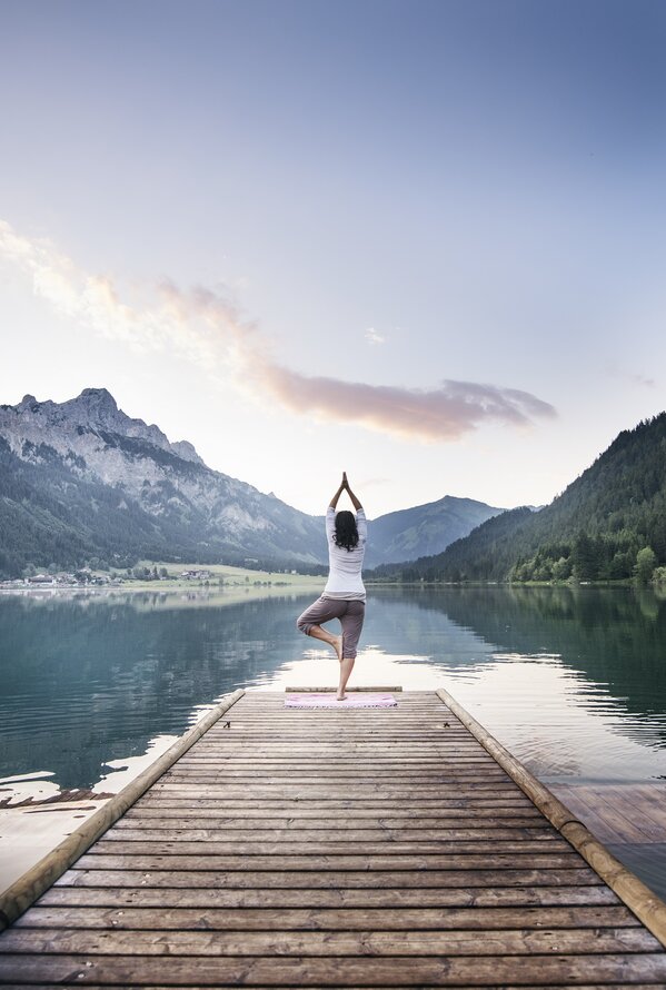 Frau macht Yoga auf Steg vor Bergsee