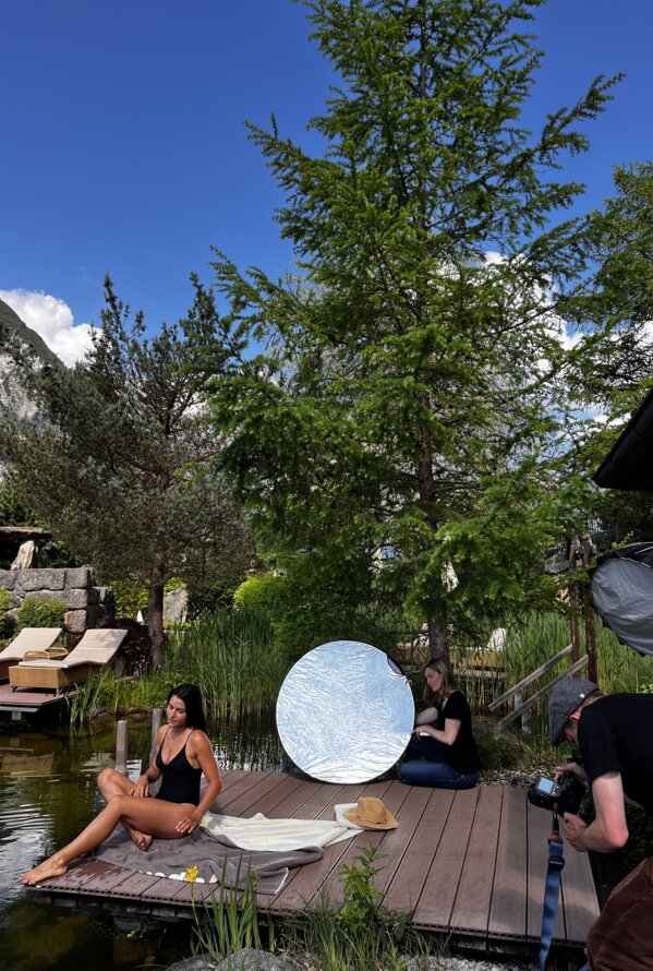 Frau im Badeanzug sitzt am See, umgeben von Bäumen und Filmcrew