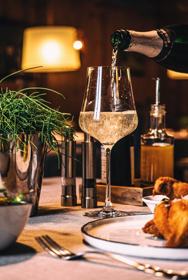 Gedeckter Tisch mit Salat, Schnitzel und Sekt, der in ein Glas gegossen wird