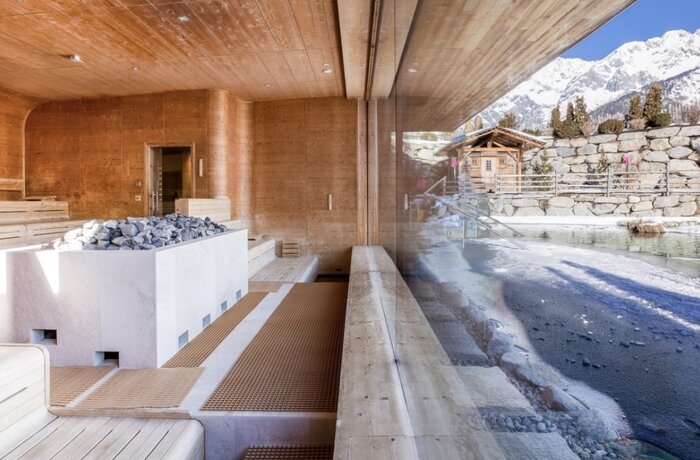 Holzverkleideter Innenraum mit Sauna und Blick auf schneebedeckte Berge und Holzhütte