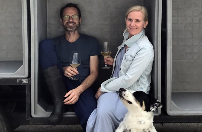 Mann, Frau und Hund sitzen in grauen Boxen mit Weingläsern