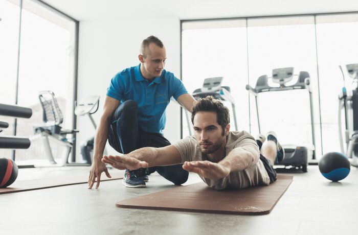 Mann macht Übung auf Matte, Trainer beobachtet