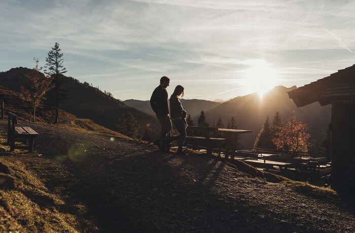 Silhouette eines Paares auf einem Hügel mit Blick auf eine Berglandschaft im Sonnenuntergang