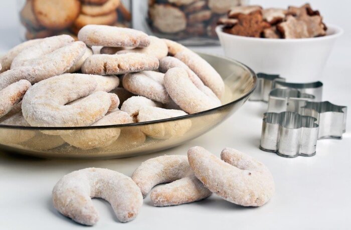 Vanillekipferl in Glasschale, mit Puderzucker bestäubt, Ausstechformen im Hintergrund