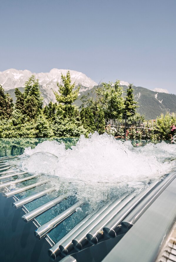 Sprudelndes Wasser im Pool vor Bergpanorama und grünen Bäumen