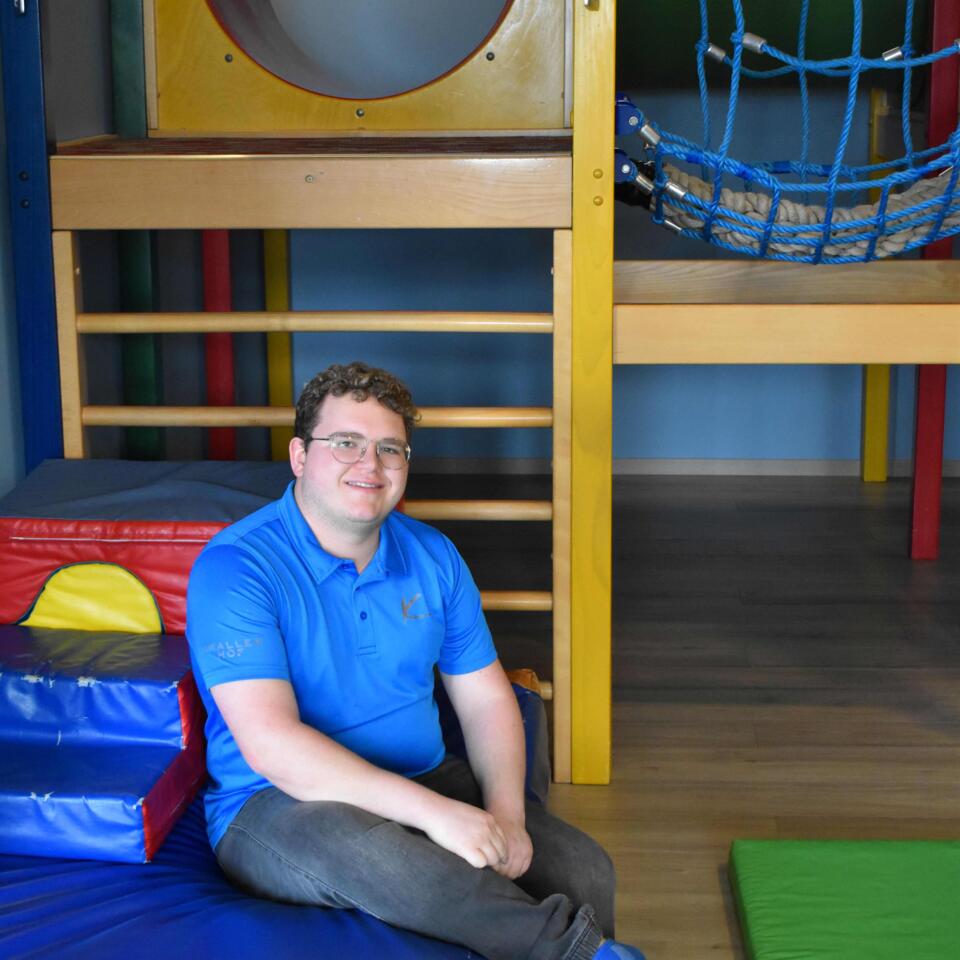 Mann mit Brille und blauem Hemd sitzt in einem Indoor-Spielplatz