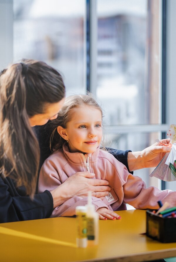 Frau hilft Mädchen am Tisch mit Bastelarbeit