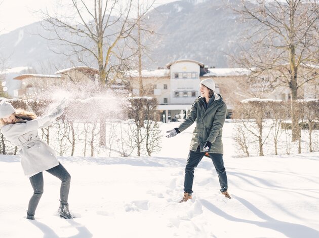 Zwei Personen liefern sich im Schnee eine fröhliche Schneeballschlacht vor einer winterlichen Bergkulisse