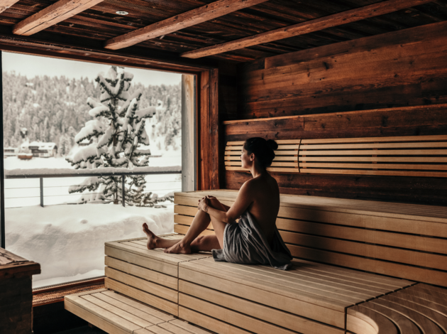 Frau entspannt in einer Sauna mit Blick auf eine verschneite Winterlandschaft.
