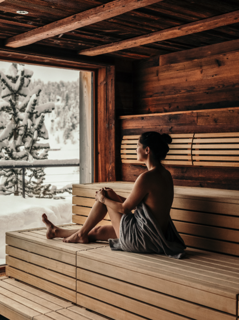Frau entspannt in einer Sauna mit Blick auf eine verschneite Winterlandschaft.