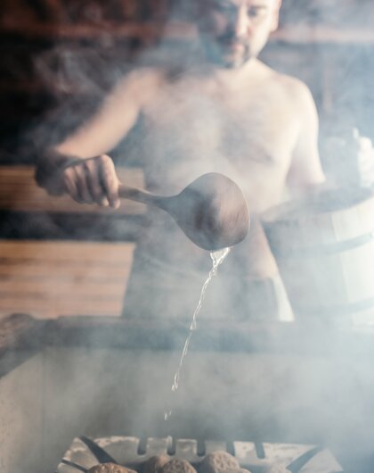 Mann beim Saunaaufguss in einer dampfenden Sauna.