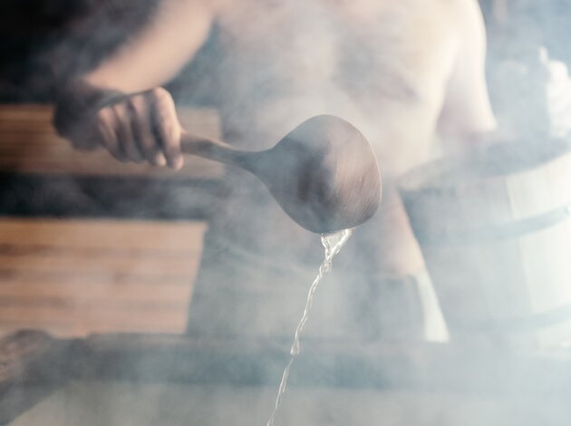 Mann beim Saunaaufguss in einer dampfenden Sauna.
