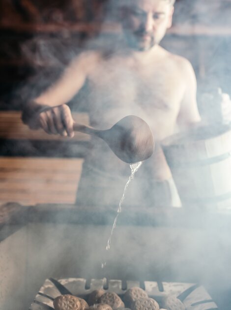 Mann beim Saunaaufguss in einer dampfenden Sauna.