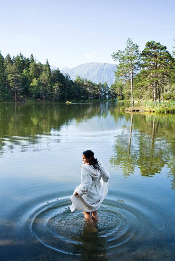 Frau im weißen Kleid steht im See, Bäume und Berge im Hintergrund