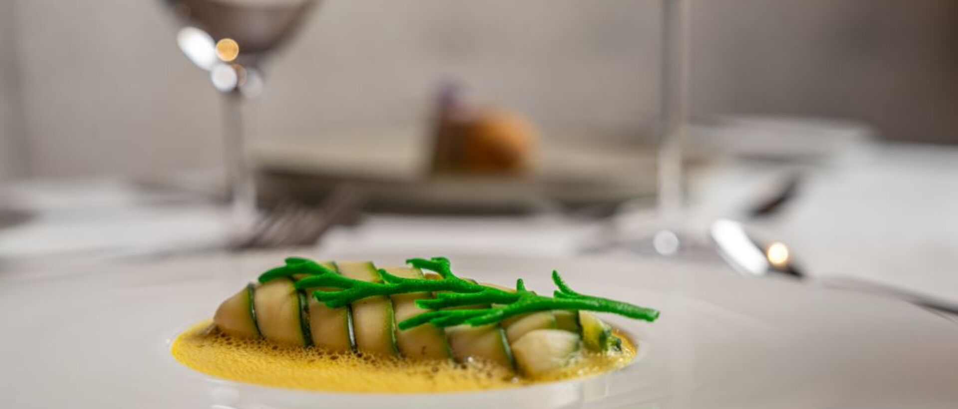 Fischgericht mit grünen Kräutern auf Teller, zwei Weingläser im Hintergrund