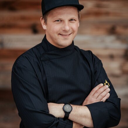 Porträt eines professionellen Küchenchefs mit moderner Kochuniform und freundlicher Ausstrahlung.