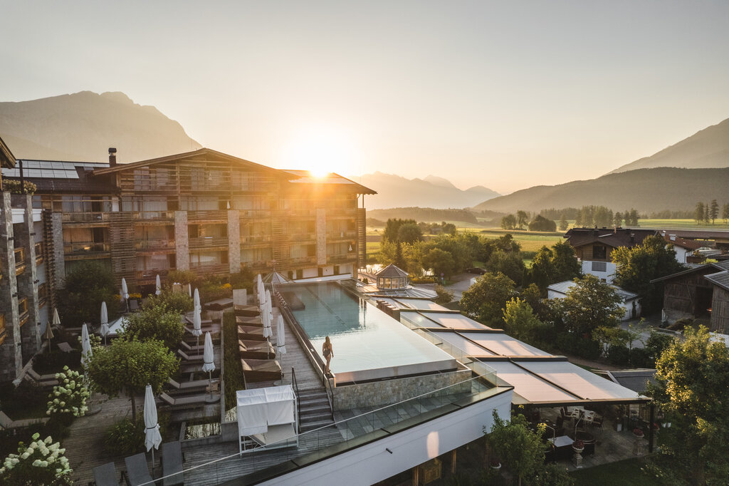 Luftaufnahme eines Hotels mit Infinity-Pool und Bergpanorama bei Sonnenuntergang
