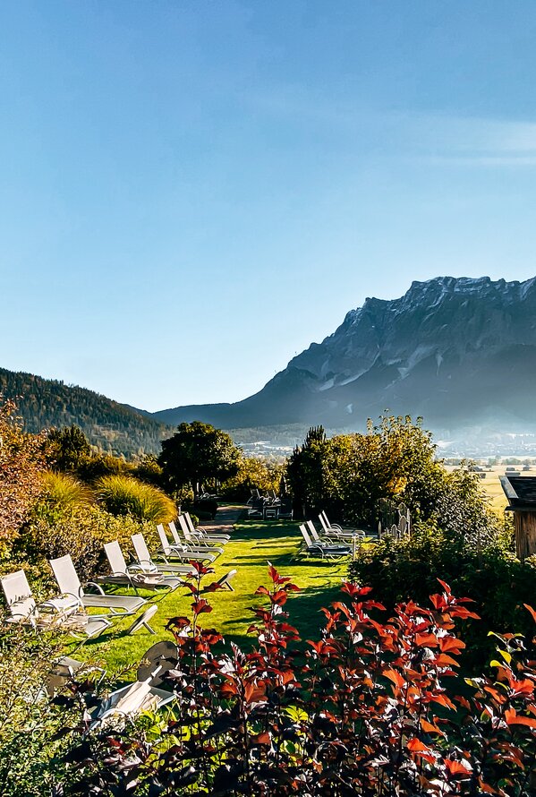 Hotel Post Lermoos mit Liegestühlen im Garten vor Bergpanorama unter blauem Himmel