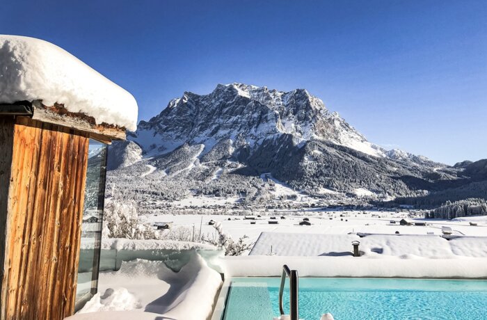 Winterlicher Solepool mit Blick auf die schneebedeckte Zugspitze unter blauem Himmel