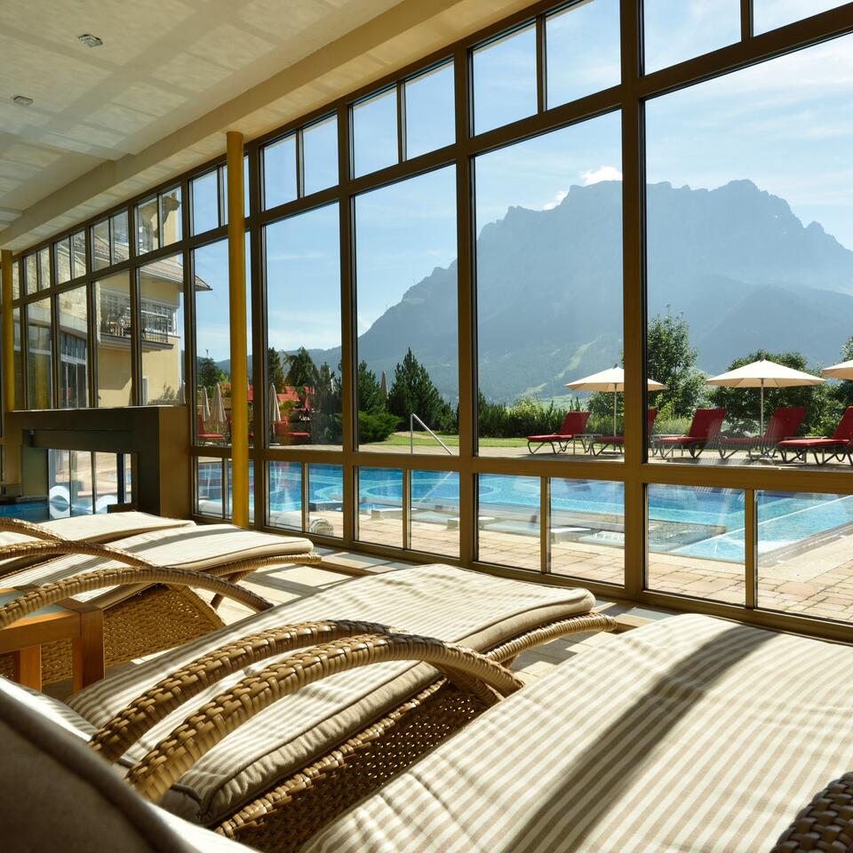 Ruheraum mit Liegen und großer Glasfront; Blick auf Pool und Bergpanorama