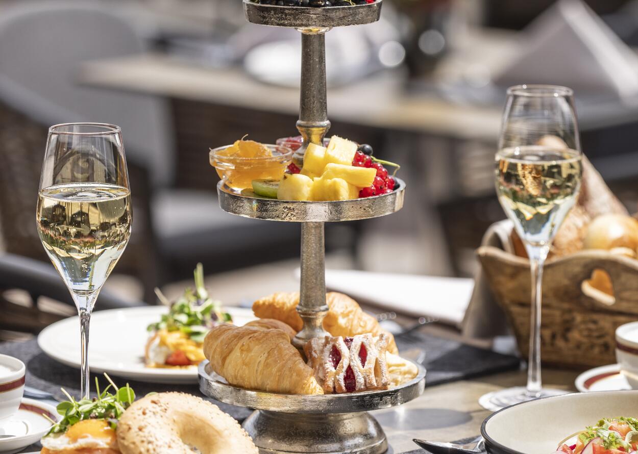 Eleganter Brunch mit Etagere, Gebäck, Obst und zwei Gläsern Sekt in stilvollem Ambiente.