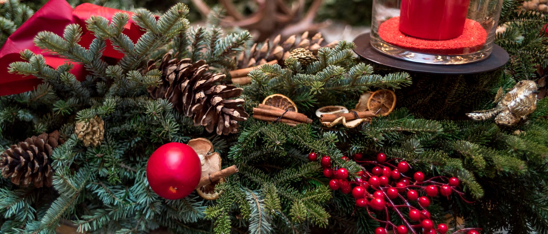 Adventskranz mit Tannengrün, Zapfen, roten Beeren, roter Kugel und Kerze unter Glasglocke