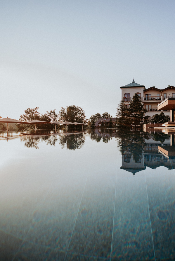 Ein ruhiger Pool spiegelt ein Hotel und den Abendhimmel wider.