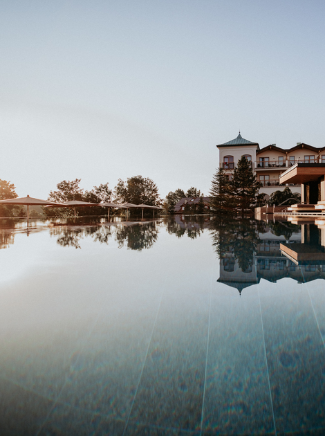 Ein ruhiger Pool spiegelt ein Hotel und den Abendhimmel wider.
