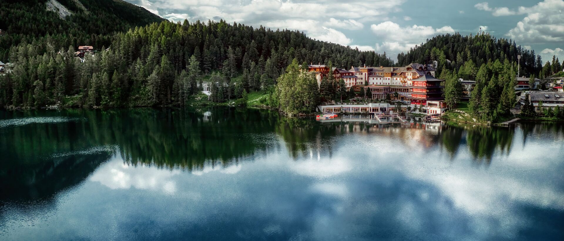See mit Spiegelung von Wolken, Wald und Häusern am Ufer