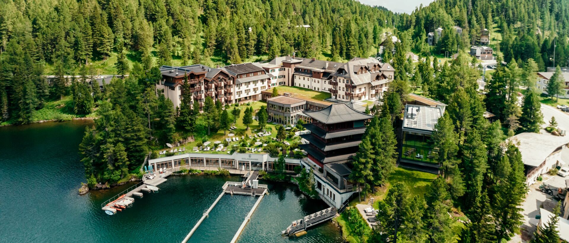 Ein luxuriöses Hotelresort liegt idyllisch an einem klaren Bergsee, umgeben von Wäldern und Bergen.