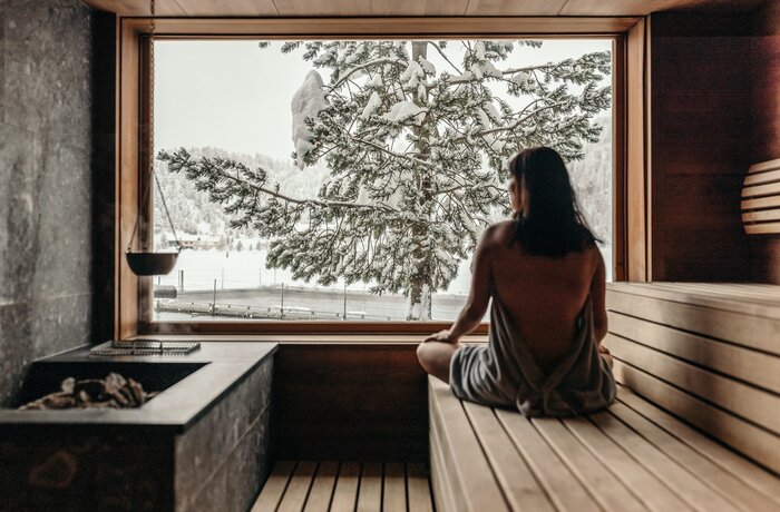 Frau in Sauna blickt auf verschneite Landschaft