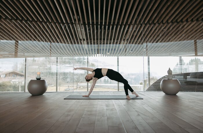 Frau macht Yoga in hellem Raum mit Holzdecke und Panoramafenster