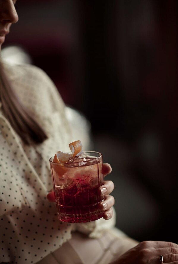 Frau hält Cocktailglas mit Eiswürfeln und roter Flüssigkeit