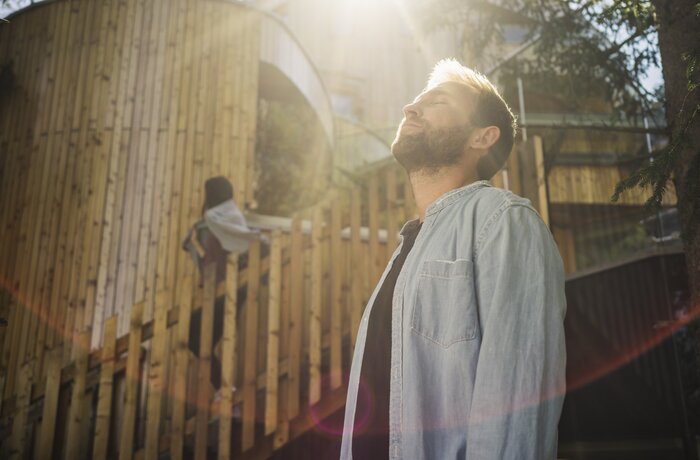 Mann mit Bart steht im Sonnenlicht vor Naturhotel Waldklause