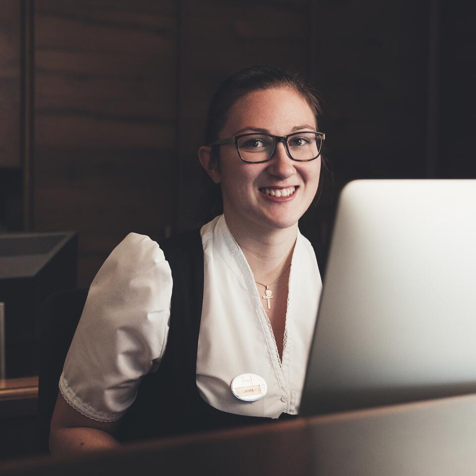 Rezeptionistin mit Brille lächelt hinter einem Computer