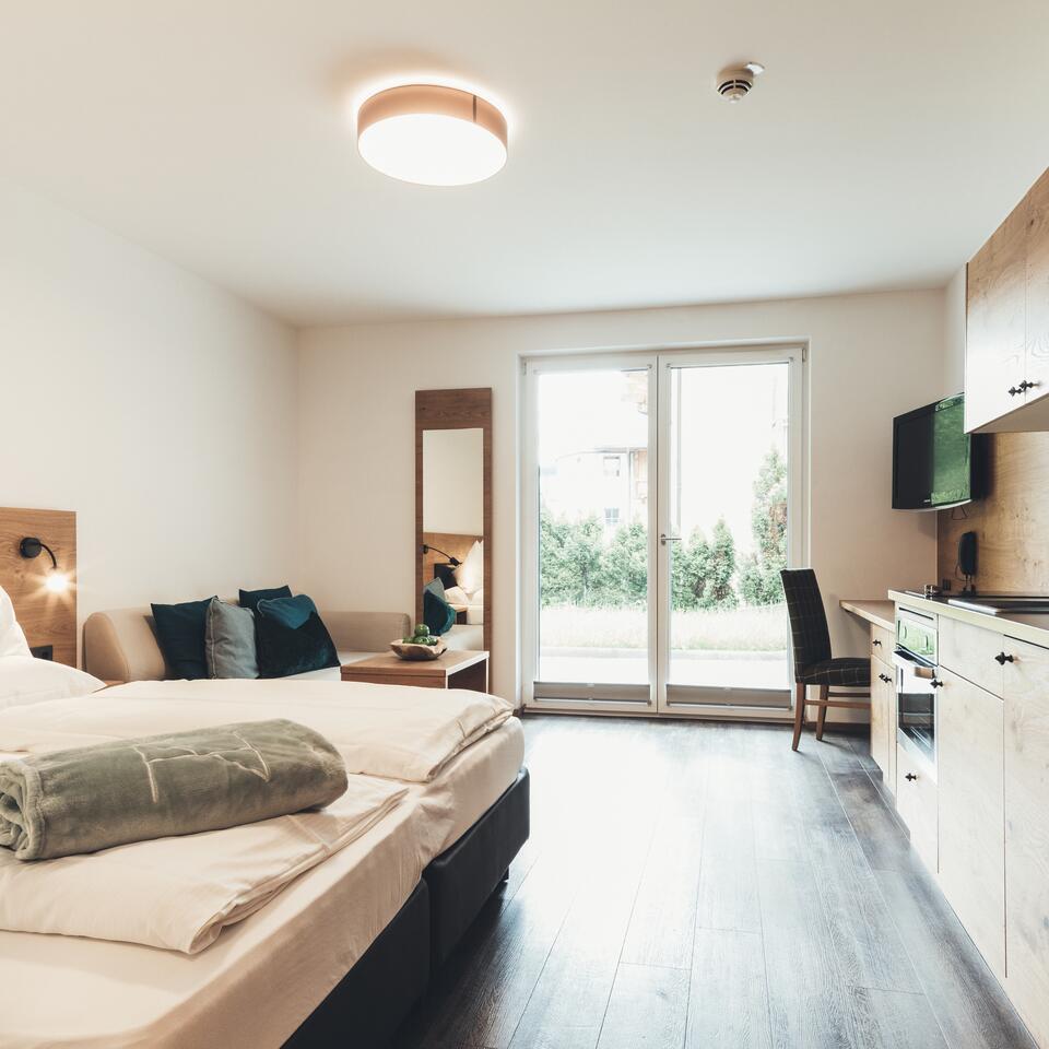 Helles Mitarbeiterzimmer mit Bett, Sofa, Schreibtisch und Zugang zum Garten