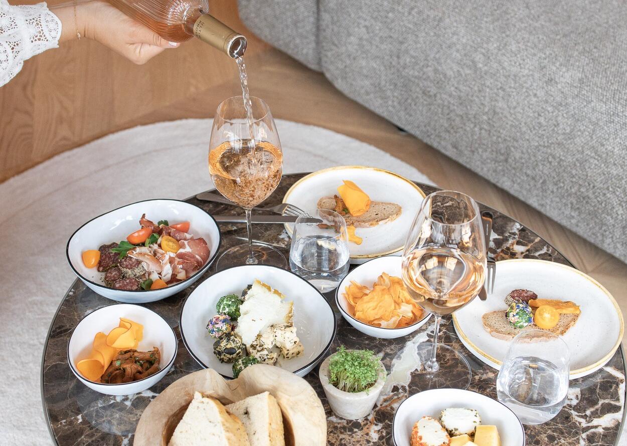 Almtapas und Roséwein auf einem Tisch, angerichtet mit Käse, Brot, Wurst und Gemüse