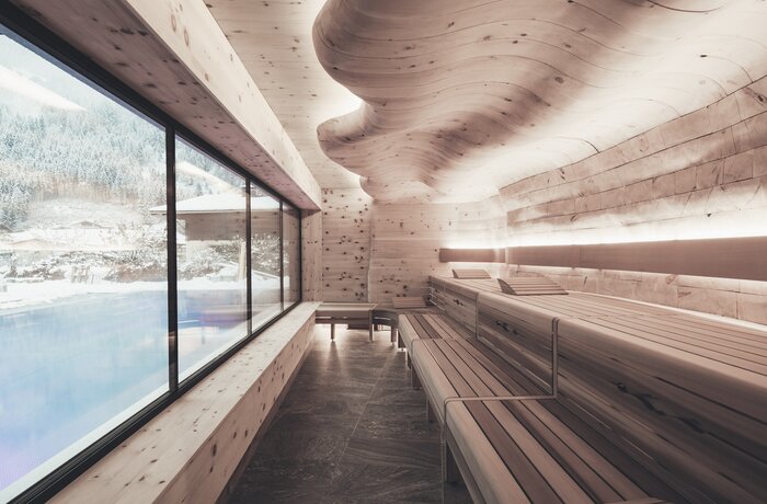 Helle Sauna mit Holzliegen, geschwungener Decke und großem Fenster mit Blick nach draußen