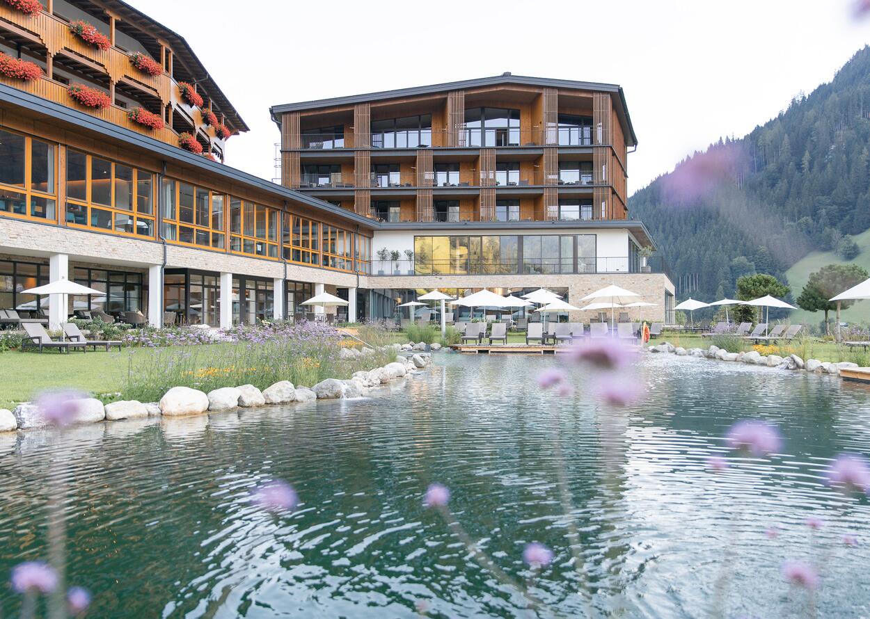 Hotel Nesslerhof mit Teich und Liegewiese im Sommer vor Bergkulisse