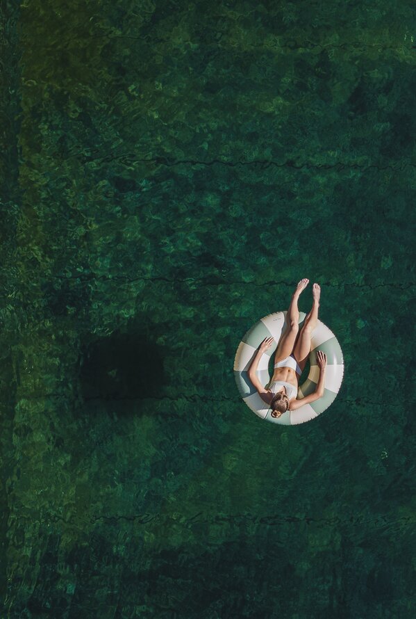 Drohnenaufnahme einer Frau auf einem Schwimmring in einem Naturpool mit klarem Wasser