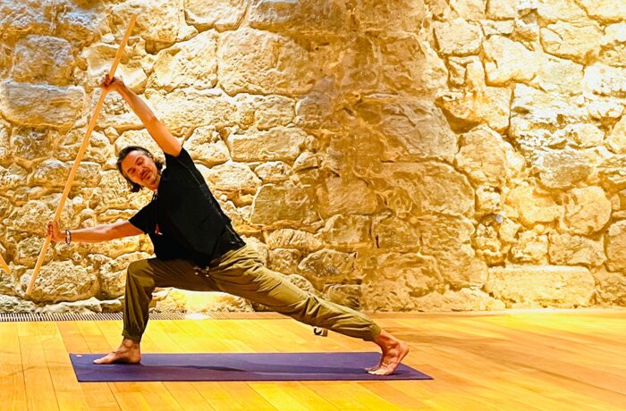 Mann macht Yoga mit Stäben vor einer Steinwand