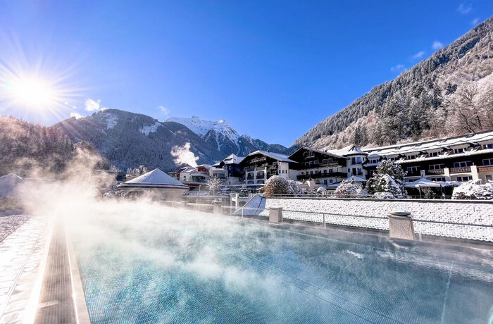 Winterlicher Pool mit Dampf, im Hintergrund verschneite Berge und Häuser am Grünberg