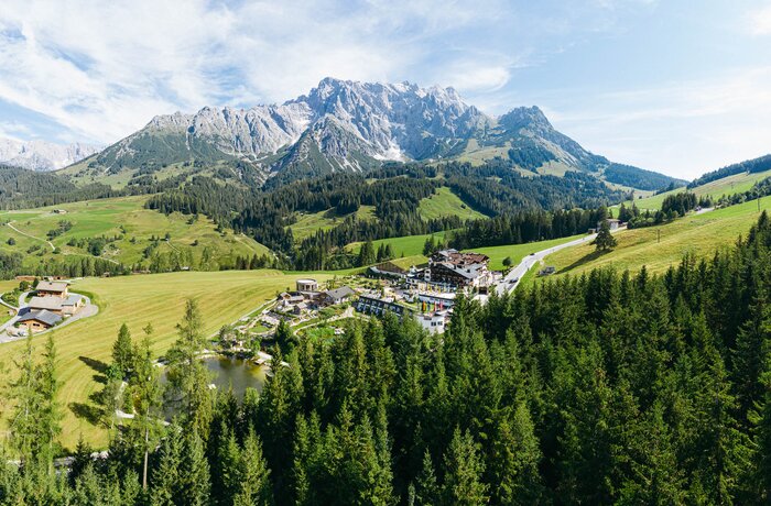 Atemberaubendes Alpenpanorama mit grünen Wäldern, sanften Hügeln und einem idyllischen Wellnesshotel mitten in der Natur.