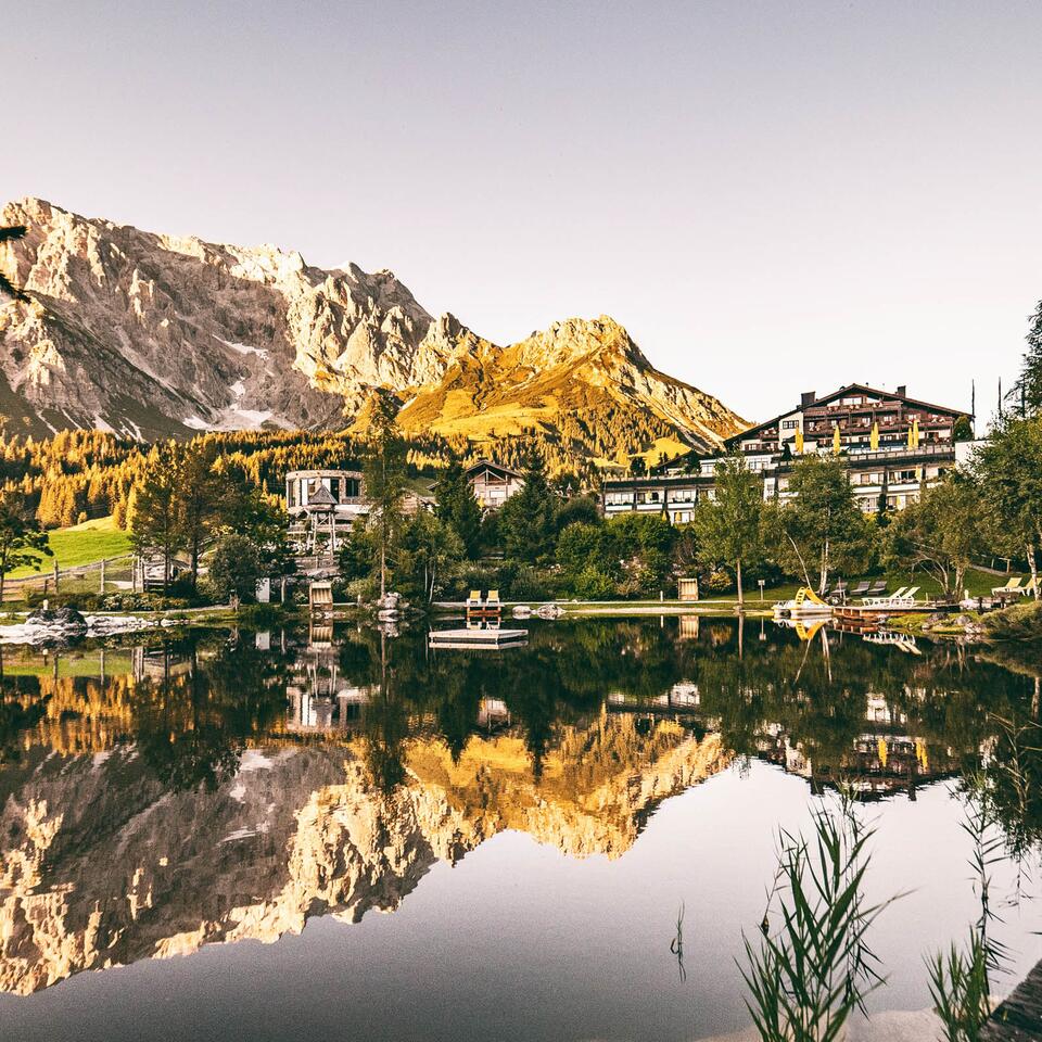 Naturpool vor Bergkulisse und Hotelanlage, Spiegelung im Wasser