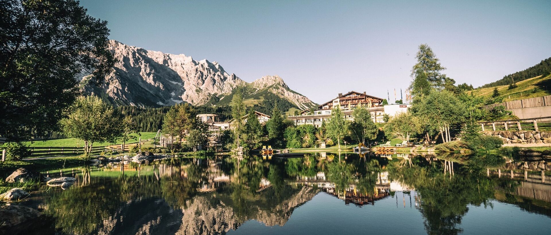 Bergsee mit Spiegelung von Bergen und Hotelanlage im klaren Wasser