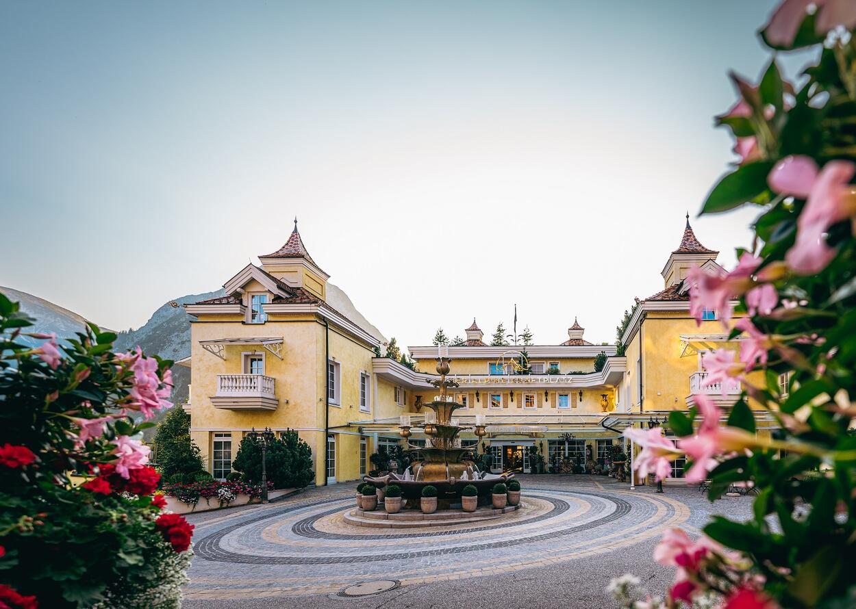 Gelbes Hotelgebäude mit Brunnen im Vordergrund, umrahmt von rosa Blüten