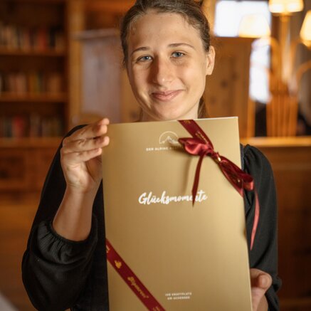 Frau hält goldene Geschenkbox mit roter Schleife