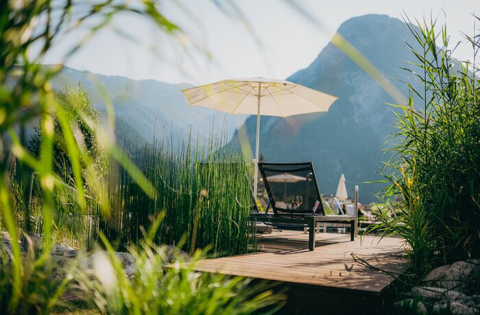 Liegestuhl und Sonnenschirm auf Holzterrasse vor Bergkulisse