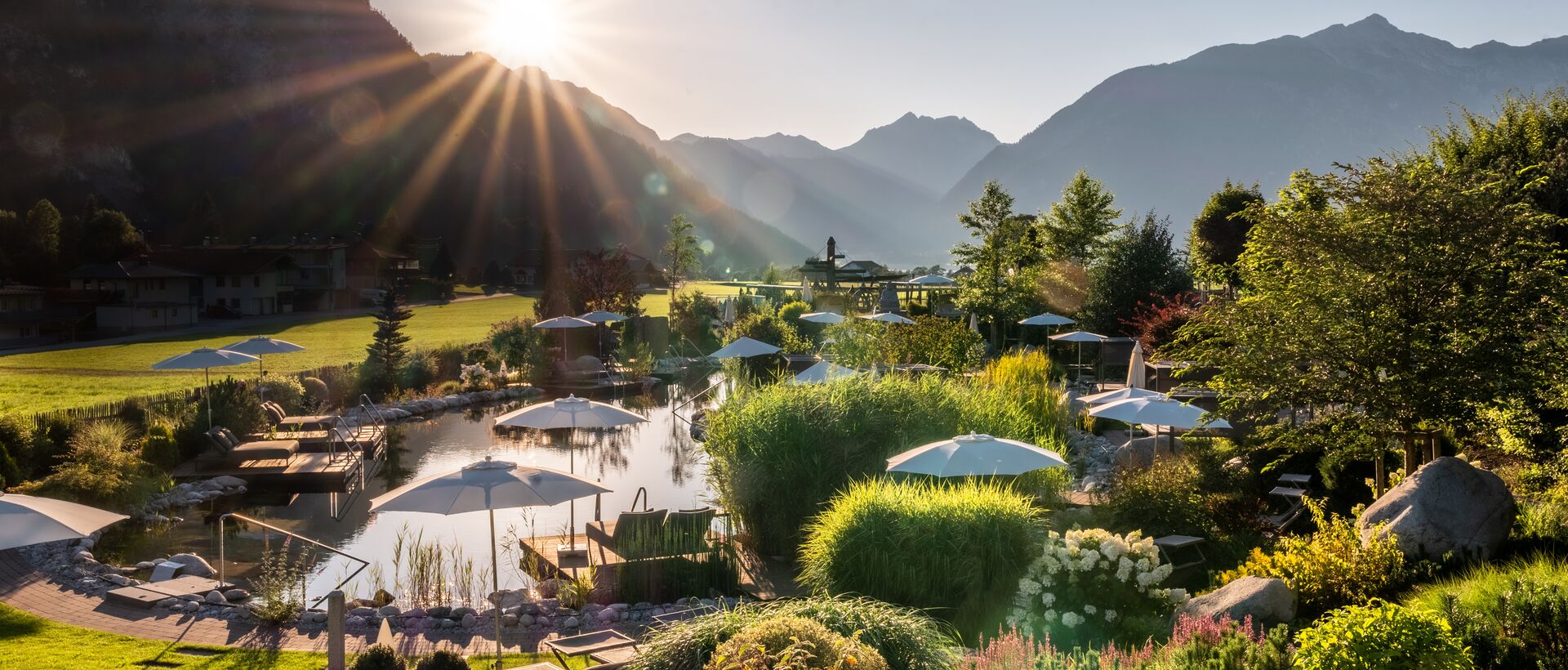 Berglandschaft mit See, Liegen, Sonnenschirmen und strahlender Sonne