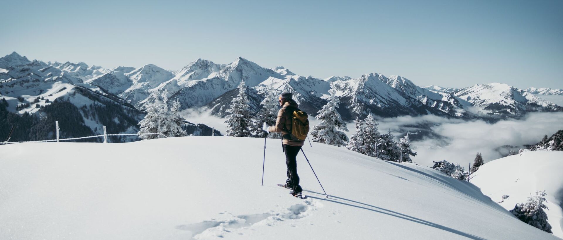 Wanderer mit Rucksack und Stöcken im Schnee vor Bergpanorama